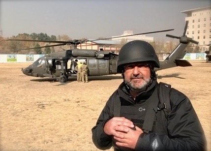 Guy Campanile in body armor and a helmet on a field assignment near a military Black Hawk helicopter
