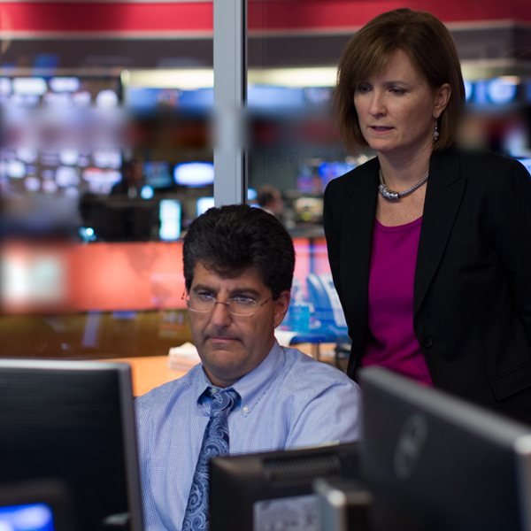 Two journalists reviewing footage together at a monitor inside a CBS News newsroom