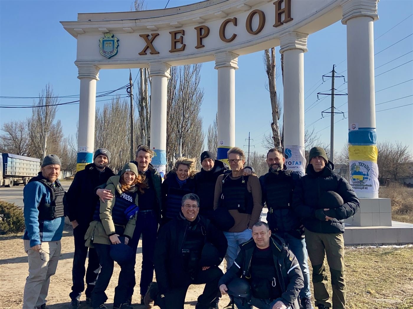 Guy Campanile and a press team in body armor at the city entrance arch in Kherson, Ukraine